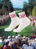 A pair of white golf socks with the brand name 'Saps' written in red, displayed against a golf course background with spectators. #color_red