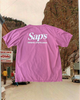 A dusty red t-shirt with 'Saps Original Sports Drink' printed on the back, displayed in a outdoor setting with a mountain and a town in the background. #color_dusty-red