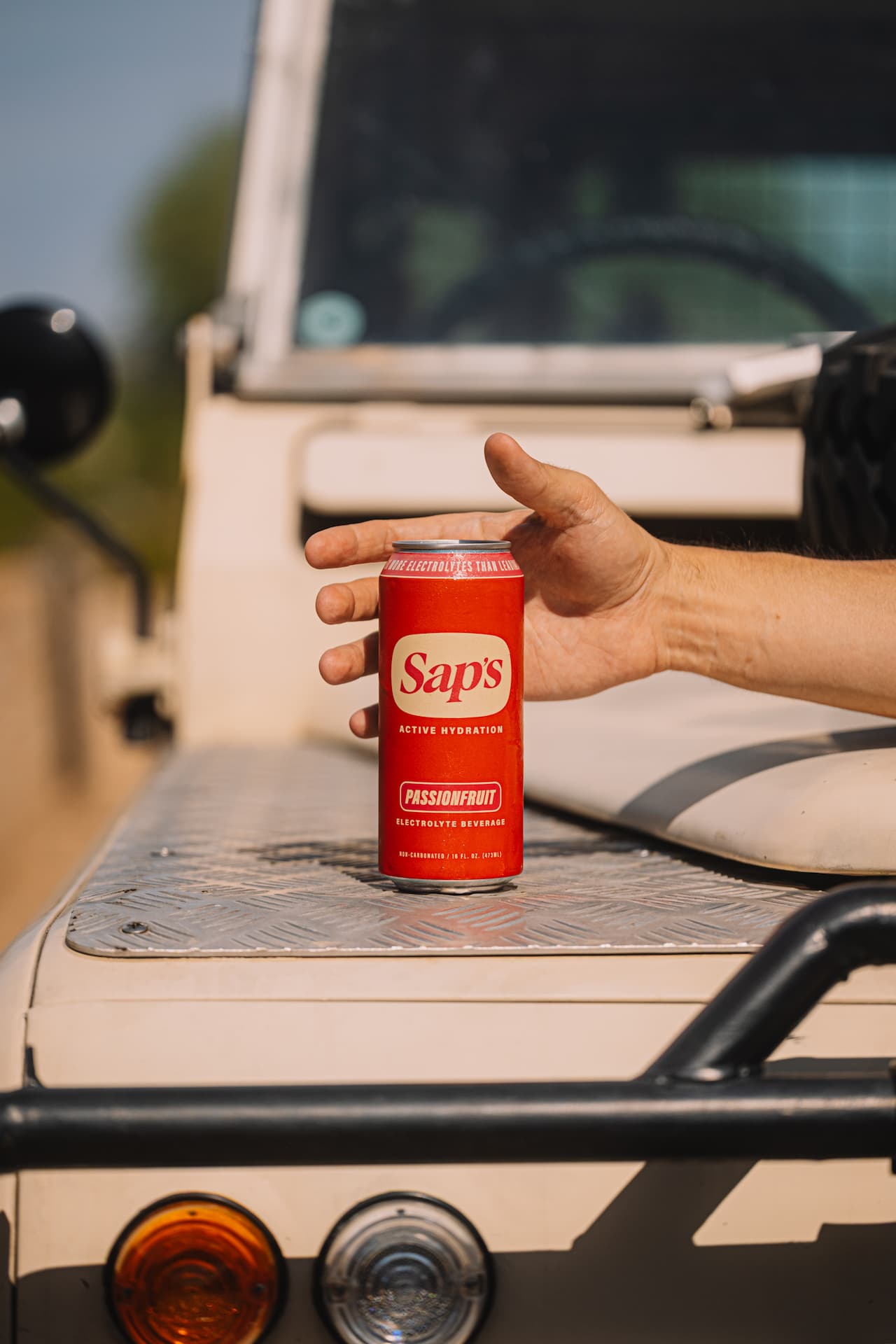 Hand holding a red Saps can on a vehicle's tailgate with a blurred background